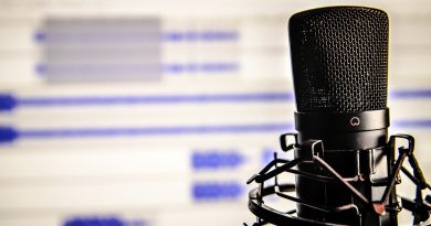 mikrofon do podcastu, w tle monitor pokazujący, że dźwięk z mikrofonu jest nagrywany